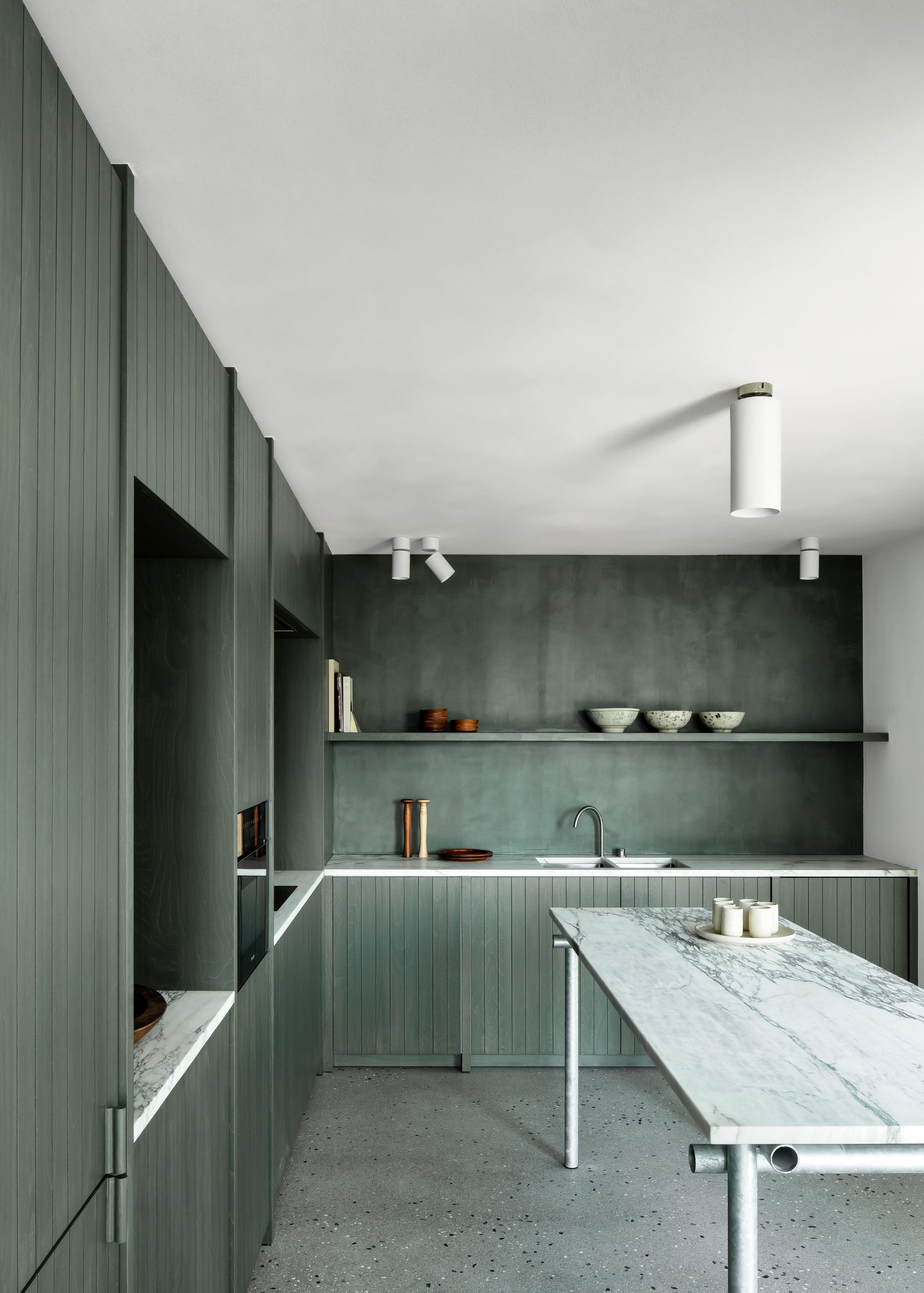 A kitchen with sage green cabinets, backsplash, and terrazzo flooring