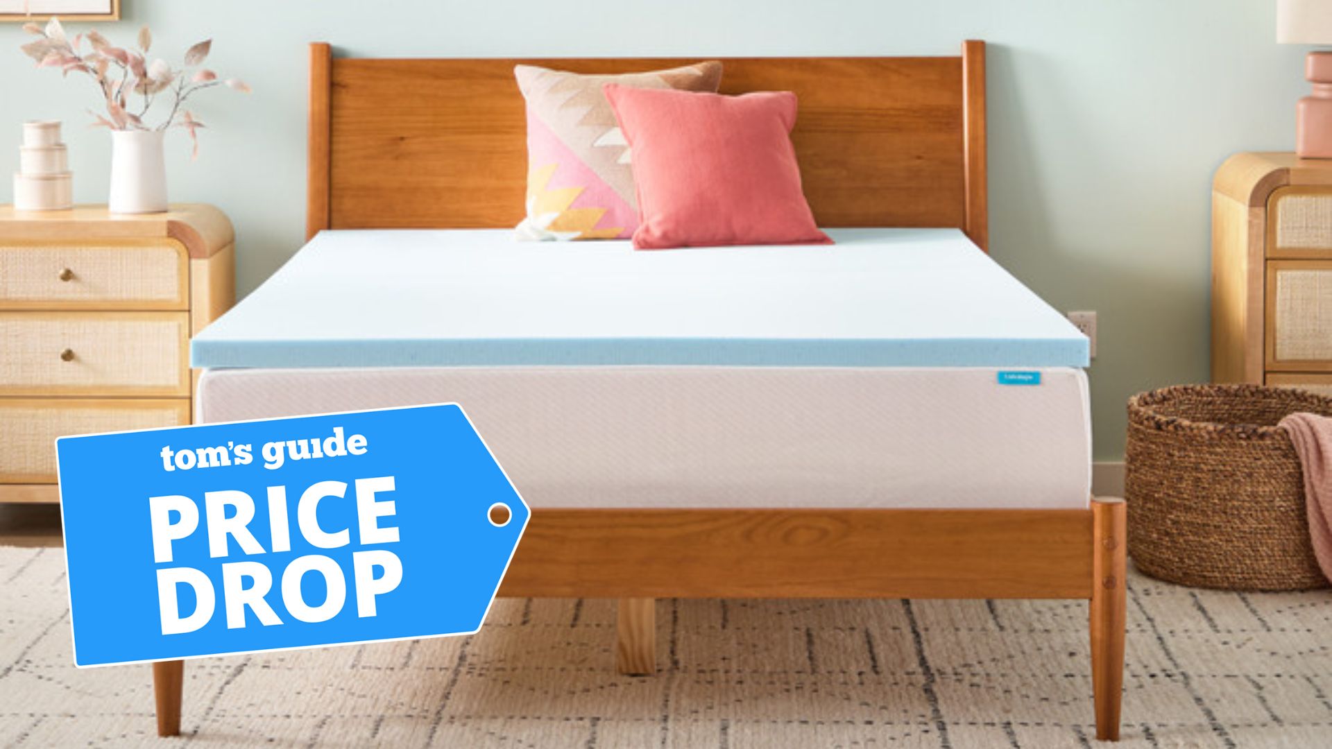 A blue Linenspa memory foam mattress topper sits on top of a white mattress on a wooden bed frame in a light, modern bedroom. A blue deals badge is in the foreground.