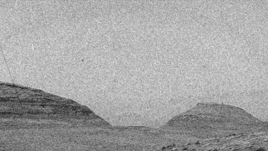 a grainy black-and-white image of a distant hill