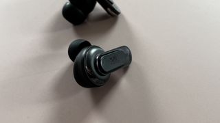 The JBL Tour Pro 2 earbuds on a pink background