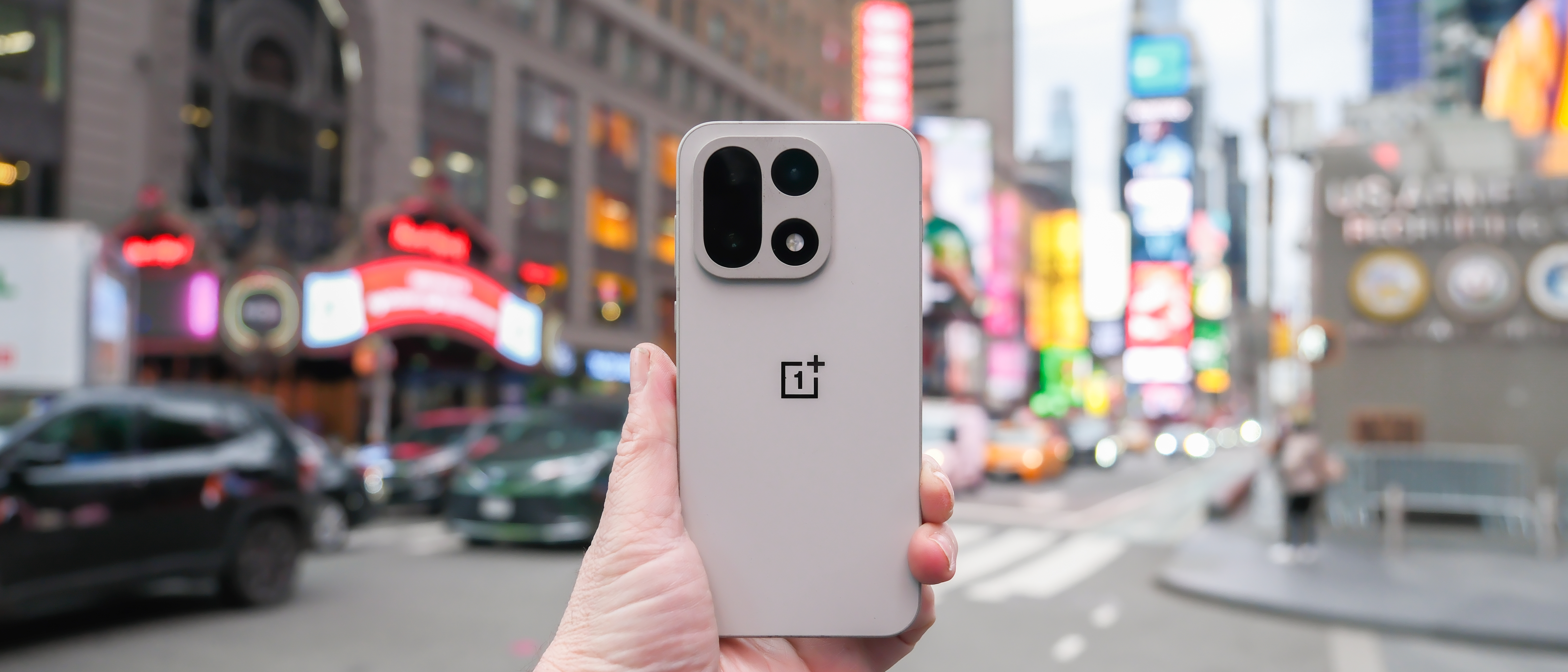 OnePlus 15 in Times Square New York City on the busy street showing the cameras and sides of the phone in addition to home screen panels and Settings menus