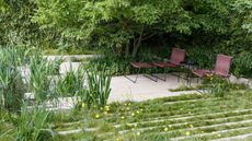 garden design with pale hardscaping and natural planting, with garden chairs and table, and trees
