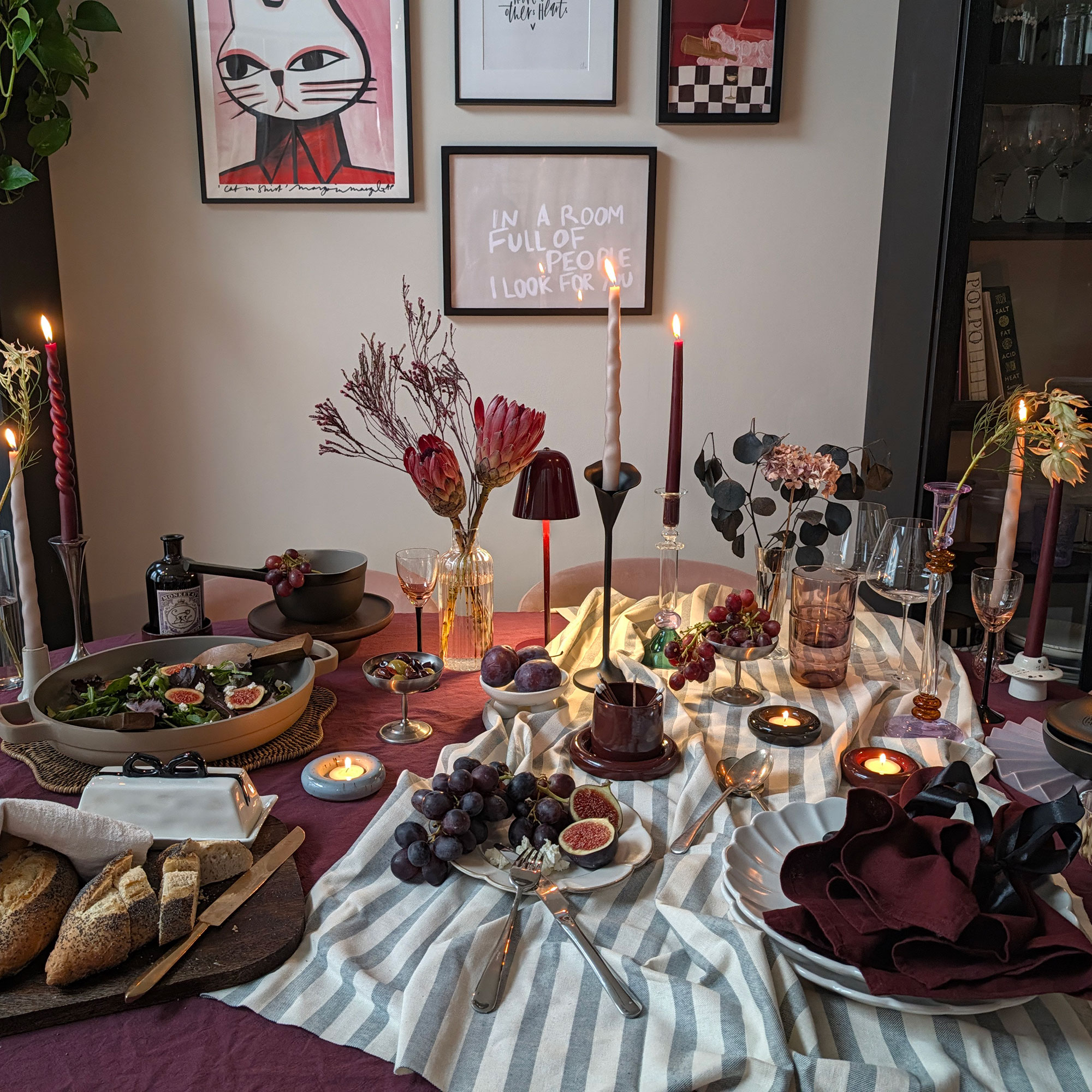 Table set for dinner party with salad bowl, bowls of fruit, lit candlesticks, wireless lamp, tealights and striped tablecloth