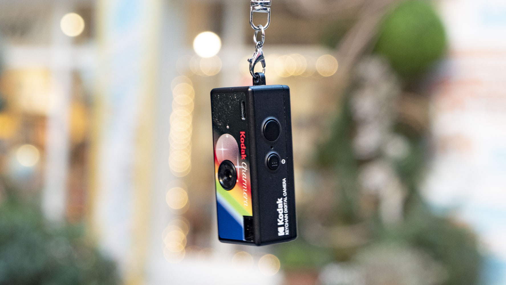 Kodak Charmera compact camera dangling from its keychain, with shop frontage backdrop