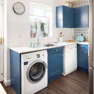 Blue kitchen with painted cabinets, chrome knobs, marble worktop, geometric tiles, wooden floor, washing machine