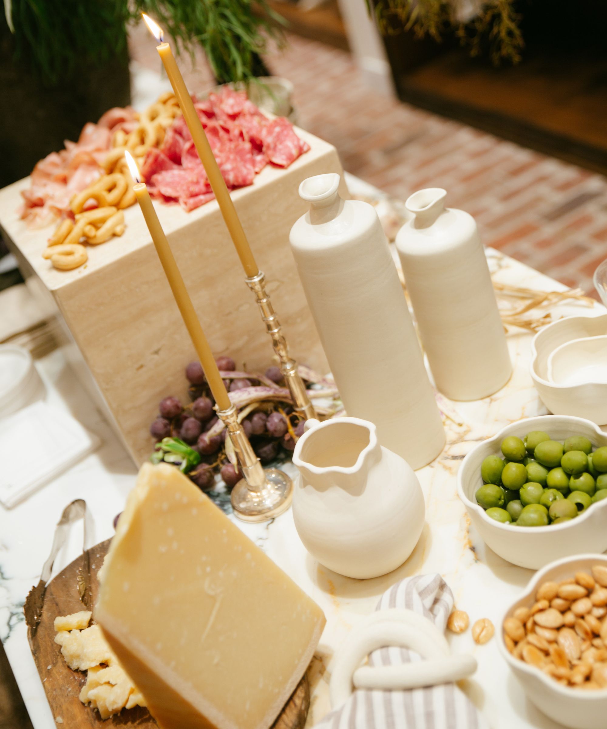 Graxing table with cheese, charcuterie and olives displayed on a marble plinth with white jugs and candlesticks
