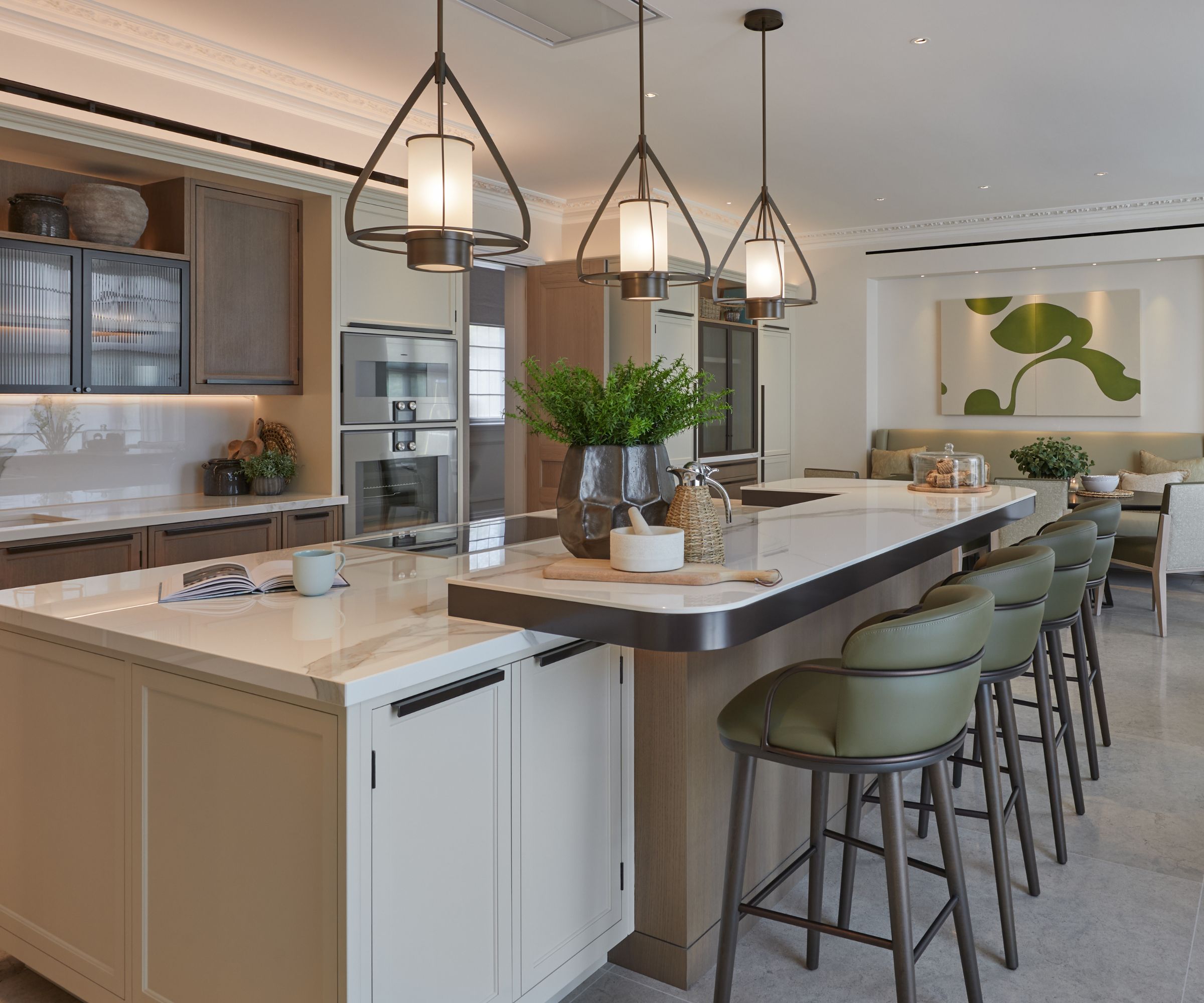 Modern kitchen with large kitchen island with seating, green leather and wood bar stools. Three pendant lights hanging over island, breakfast nook and artwork in the background to the right