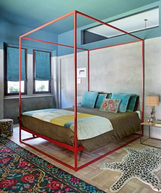 bedroom with blue ceiling and gray walls, red four poster, colorful throw and cushions, patterned rug and stool, and children's leopard rug