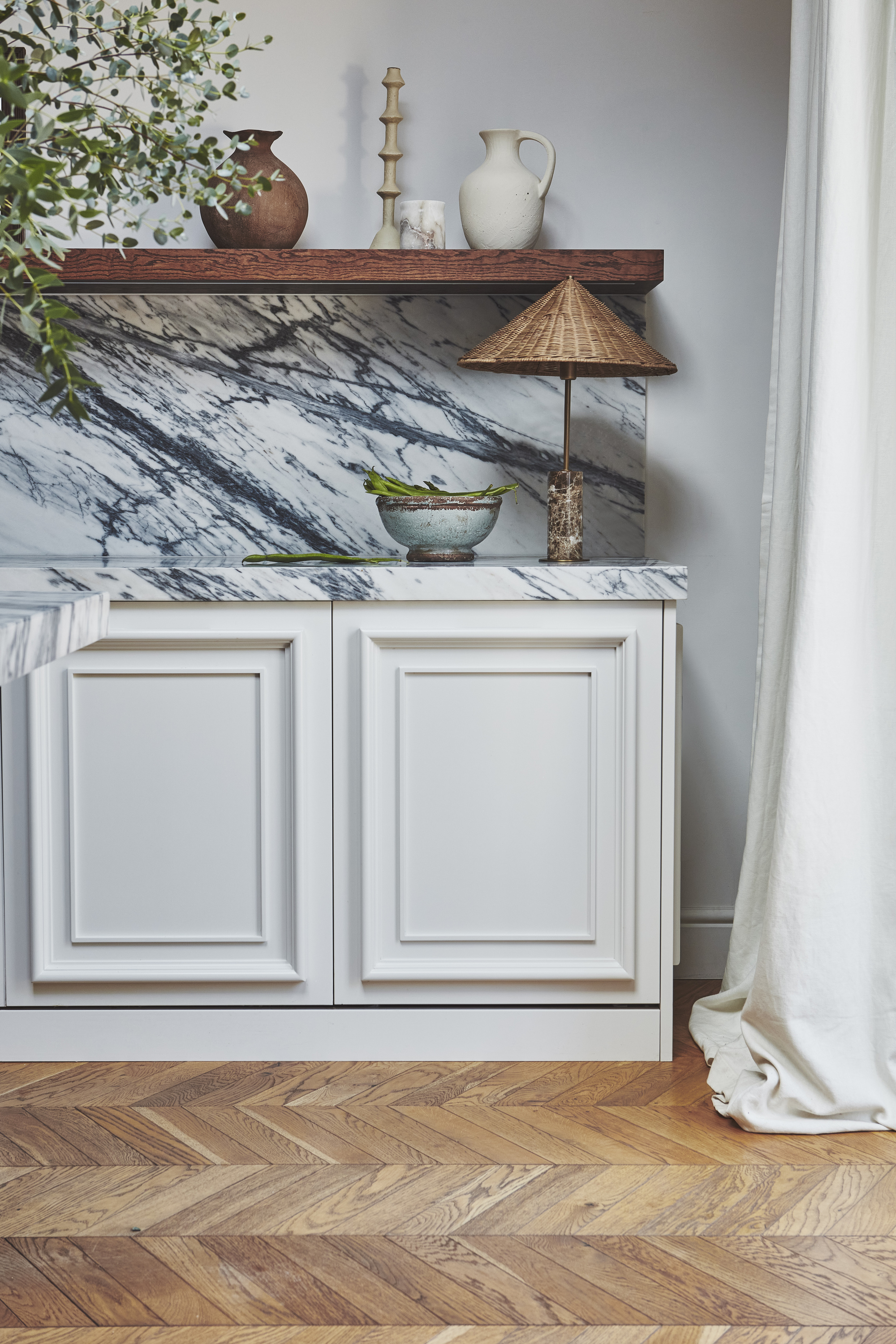 A kitchen with cream shaker cabinets, a marble backsplash, and a rattan lamp on te counter