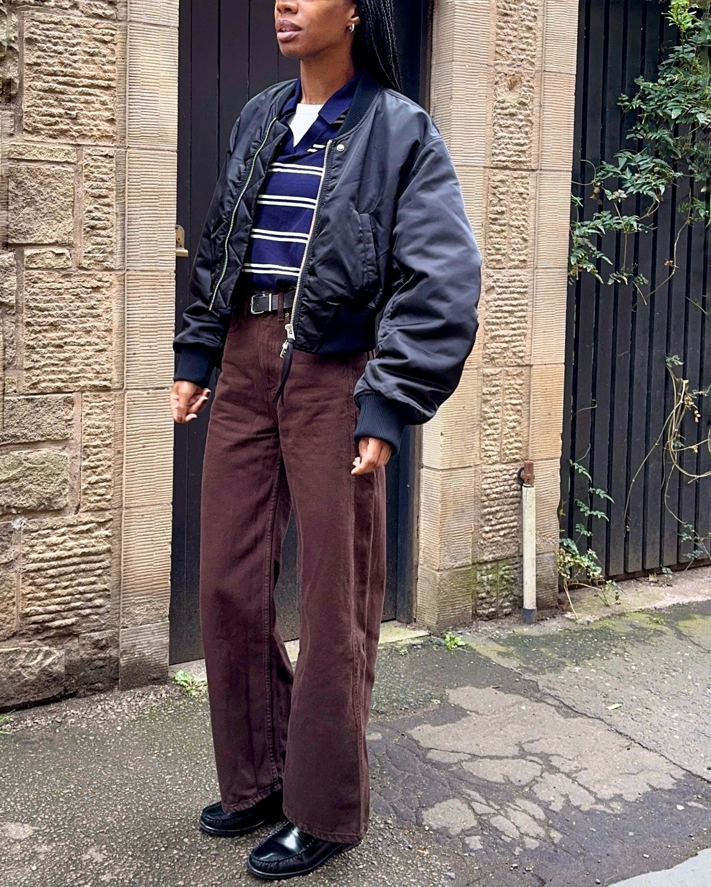 Influencer @louisahatt wears brown jeans with black glossy loafers and a navy bomber jacket.