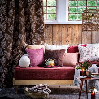 Living room with wood panelled walls, patterned curtains and daybed layered with cushions