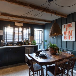 Dark kitchen with blue wood panelling and rustic table and period beams