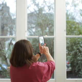 Lady in pink sweatshirt holding smartphone up to a white sash bay window