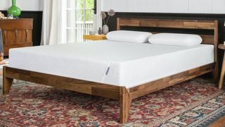 Tuft & Needle vs Casper: The Tuft and Needle Original Mattress shown on a dark wooden bed frame placed on a red tapestry-style rug
