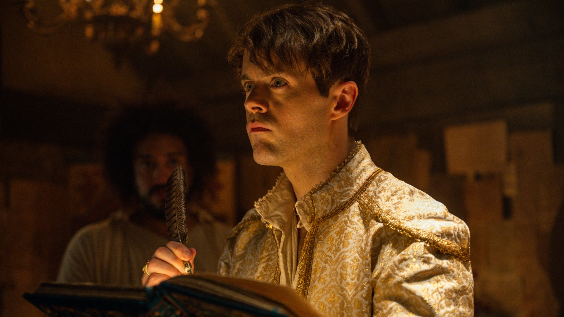 Jaskier (Joey Batey) holding a quill in The Witcher