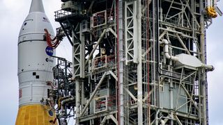 An orange rocket with a white top next to a launch tower.