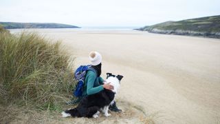 Woman sat with dog on beach looking out 