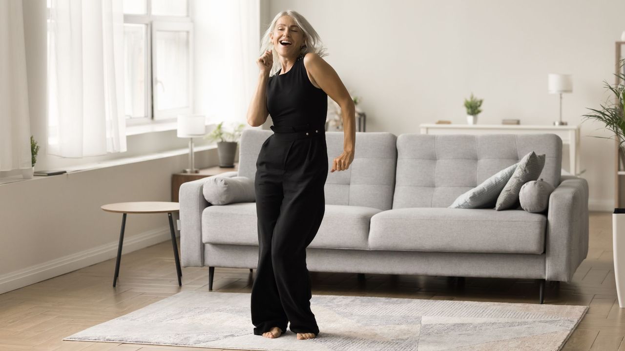 Woman dancing in living room in front of sofa to get 10,000 steps in without leaving the house