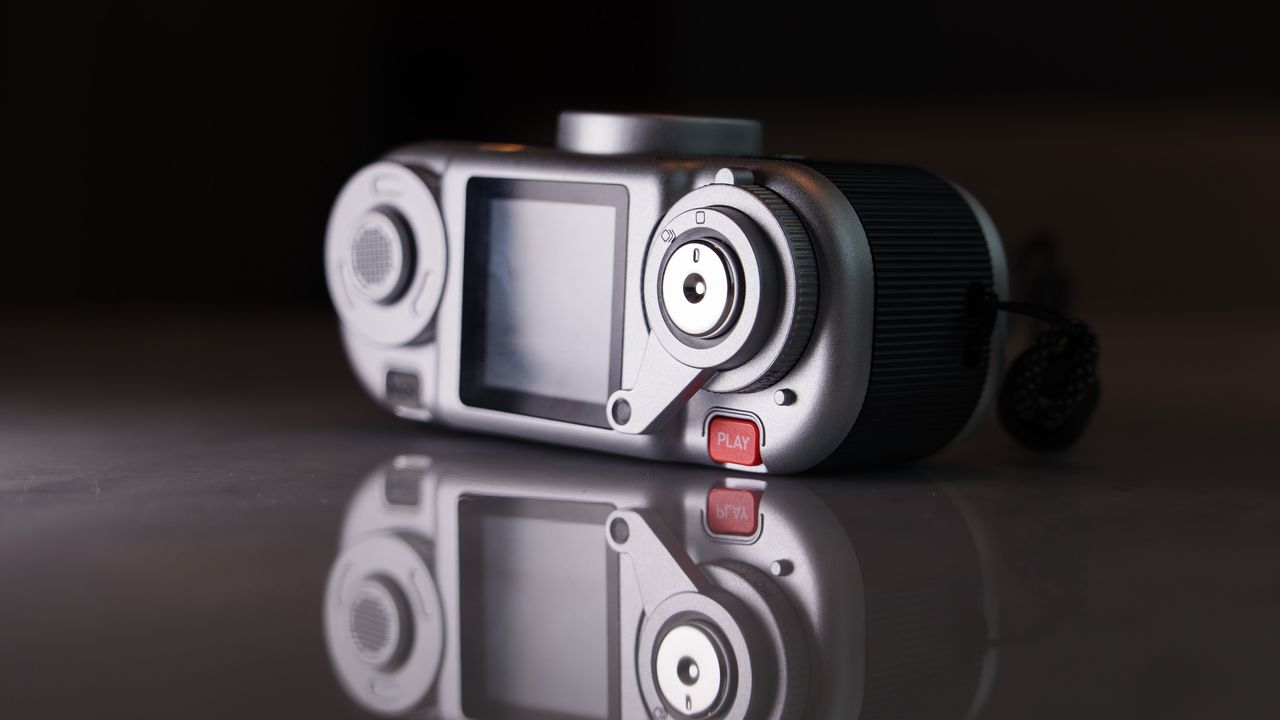 Fujifilm Instax Pal 2 digital camera on a marbled white surface, close up of the wind lever