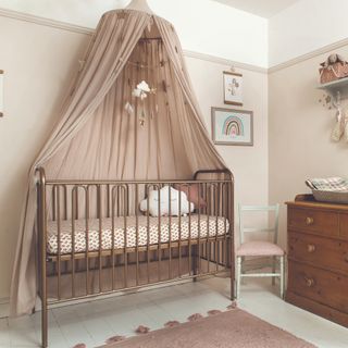 Wooden crib with soft brown canopy hanging from ceiling, next to drawers with changing unit