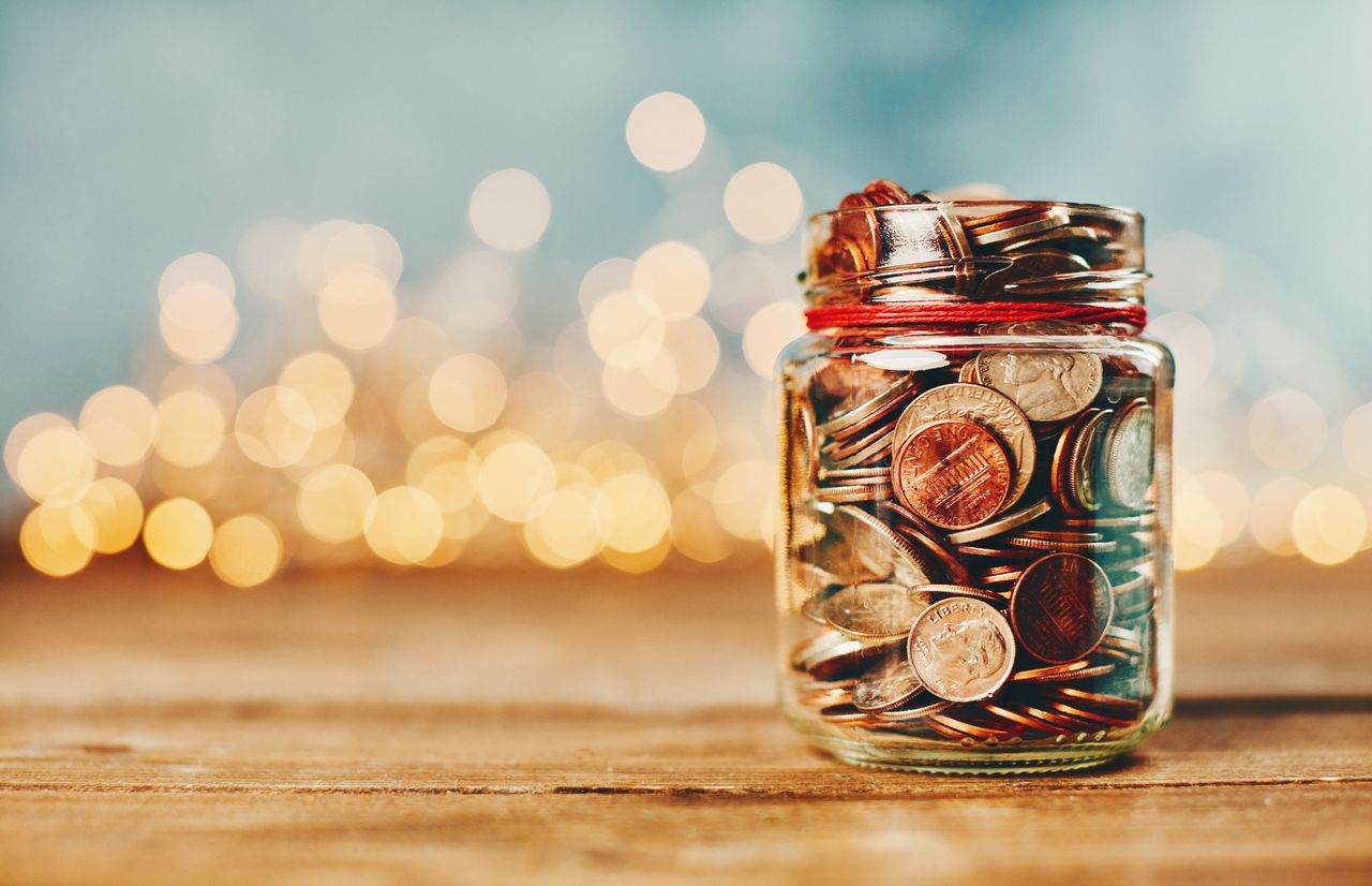 Donation money jar filled with coins in front of holiday lights