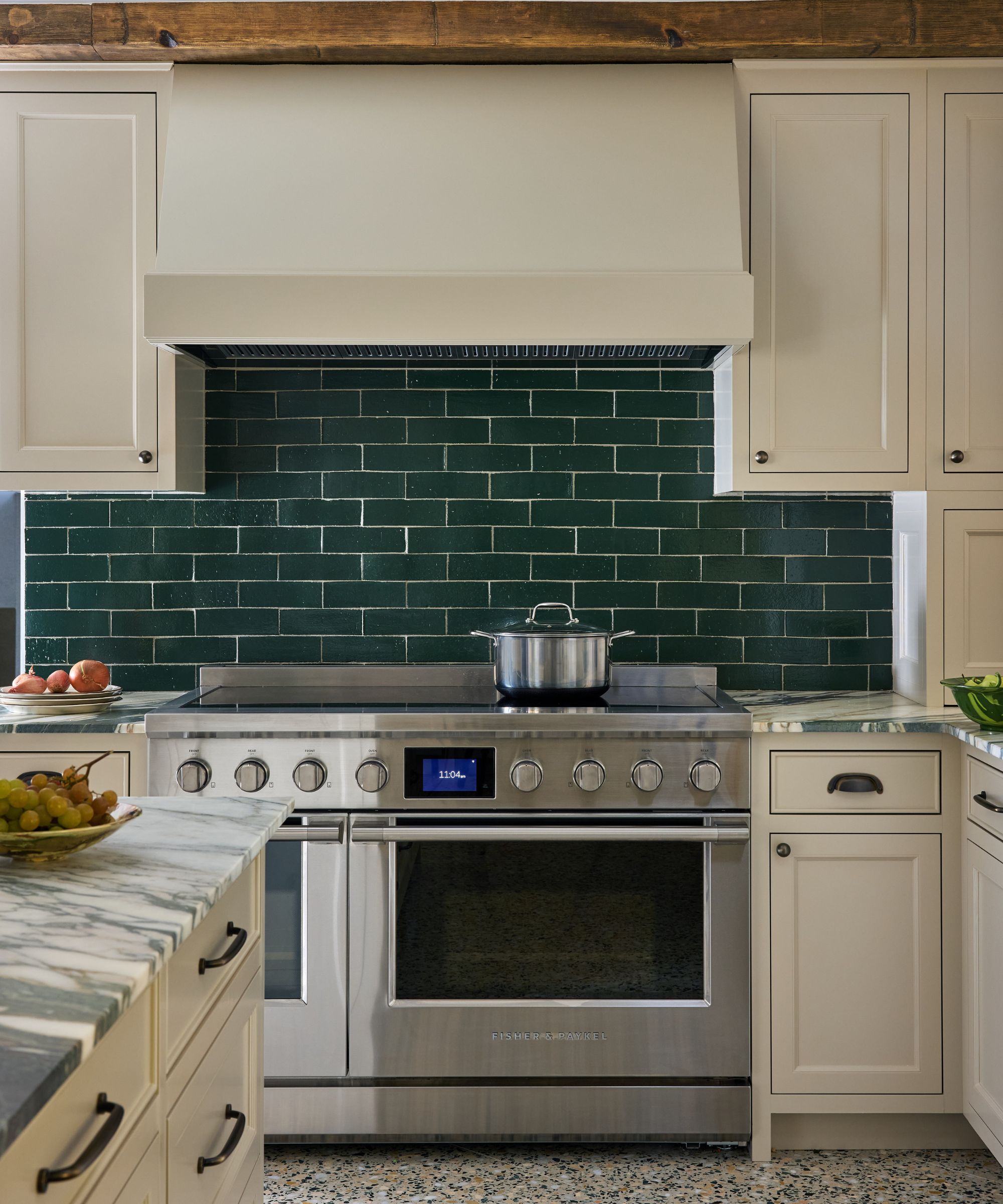 A kitchen with neutral cabinets and a silver cooker with dark green backsplash tiles.