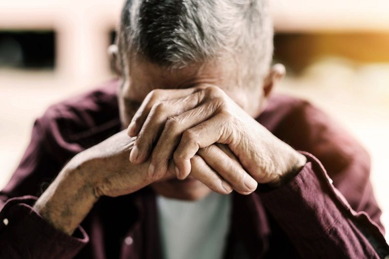 An older adult covering his face with his hands.