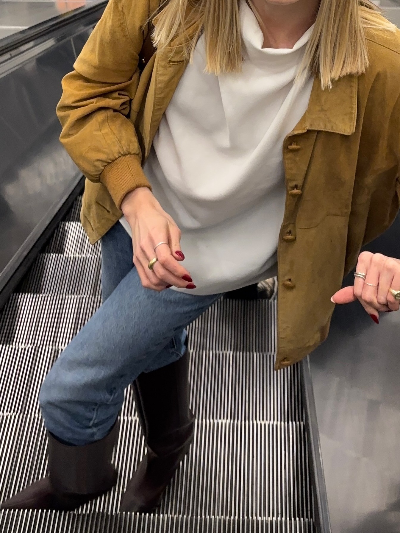 Fashion person Lou Northcote wears a tucked knee high boots trend. She wears a yellow jacket, blue jeans and brown leather knee high boots.