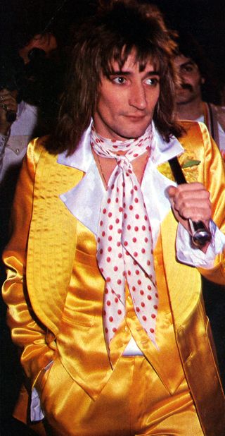 Rod Stewart, posed, wearing a yellow satin suit.
