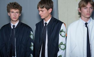 Three male models wearing clothing by Dior Homme in light and dark shades.