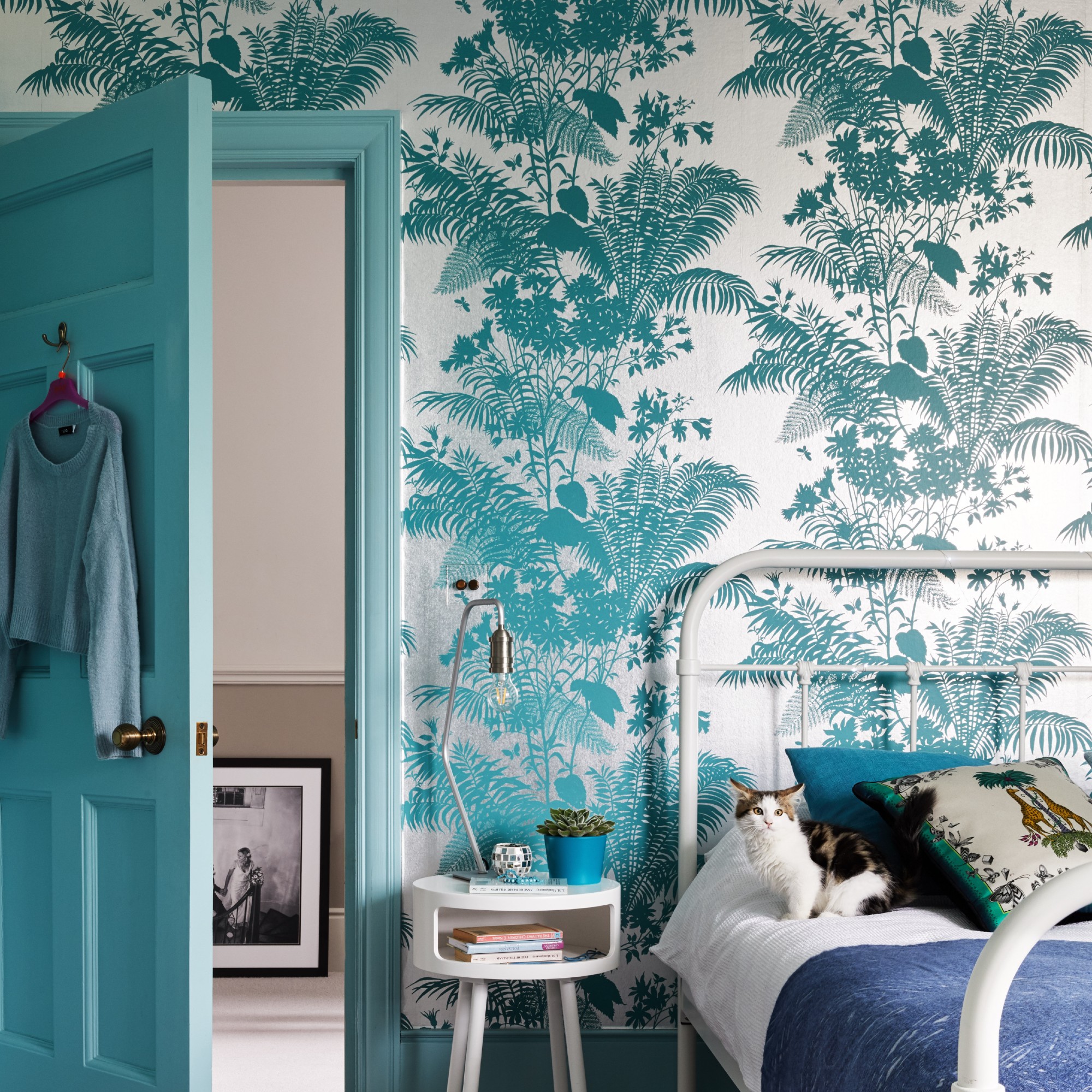 A bedroom with a bold floral wallpaper in a blue shade matching the door
