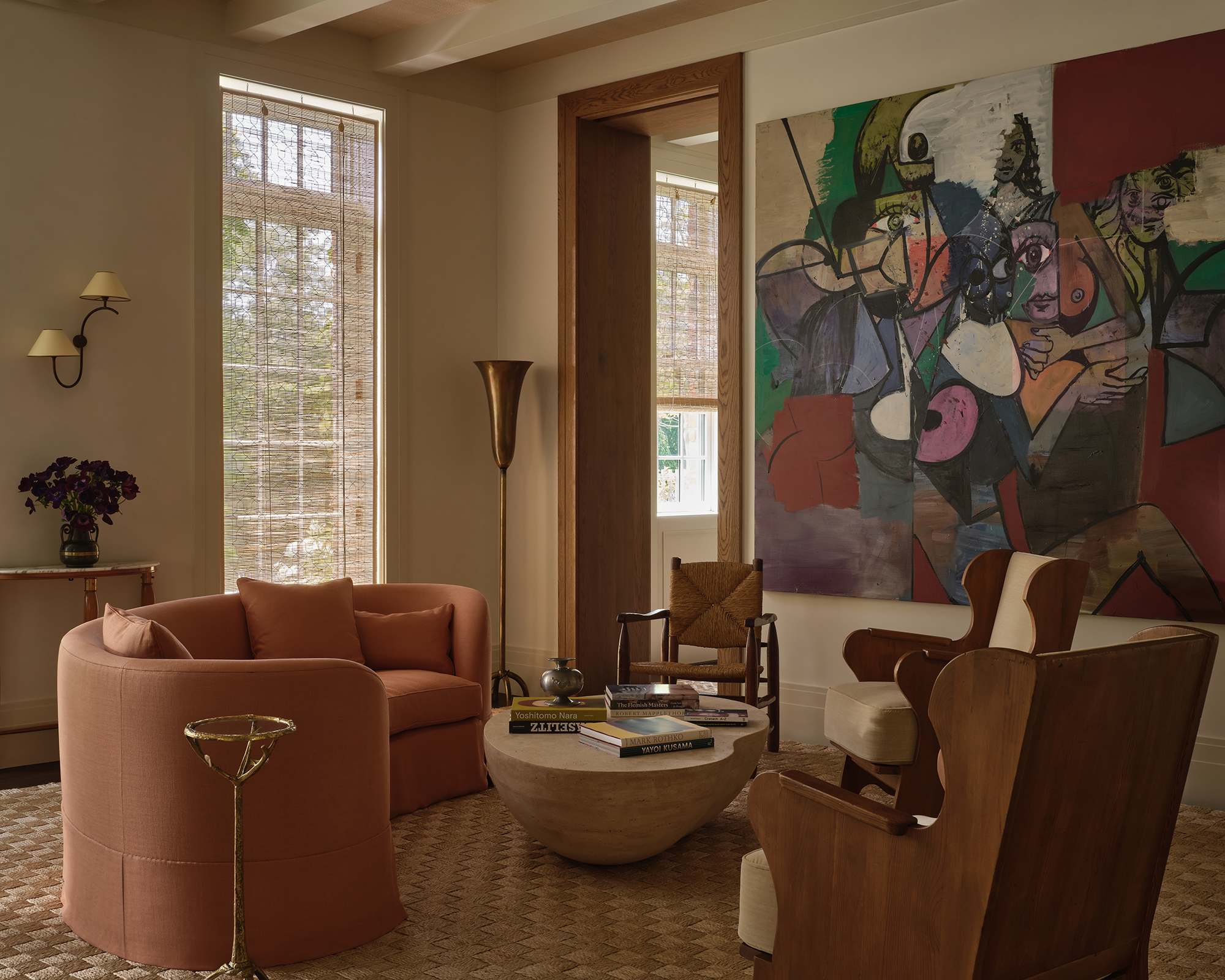 large living room with huge graphic art print on the wall a mix of chairs and a curved pink sofa angled around it on the floor