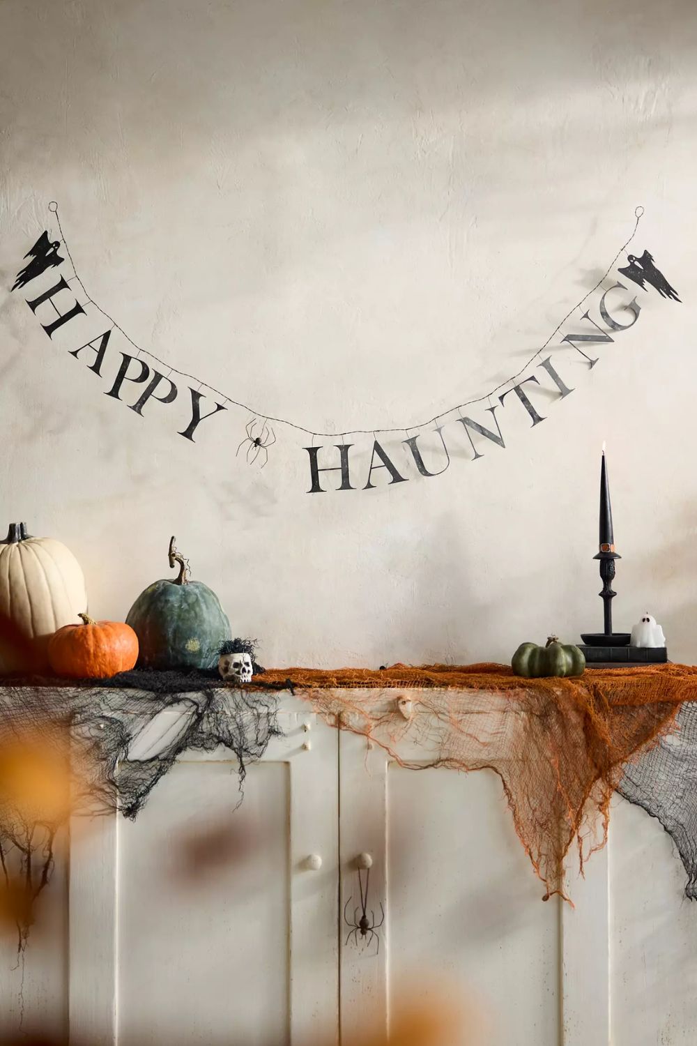 Black metal &#039;happy haunting&#039; garland above a mantel decorated with mini pumpkins