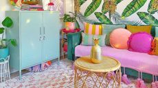 A picture of a colorful living room with a rattan coffee table, a pink couch, and leafy wallpaper