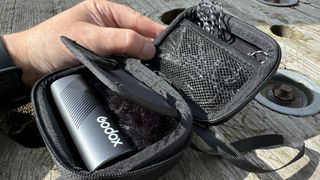 Godox Cube-SC microphone in a case held in a hand over a wooden surface