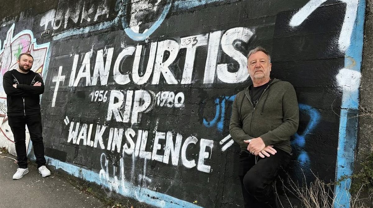 Jack Bates (left) and former Joy Division/New Order bassist Peter Hook of Peter Hook & the Light standing before a mural in tribute to the late Joy Division singer Ian Curtis