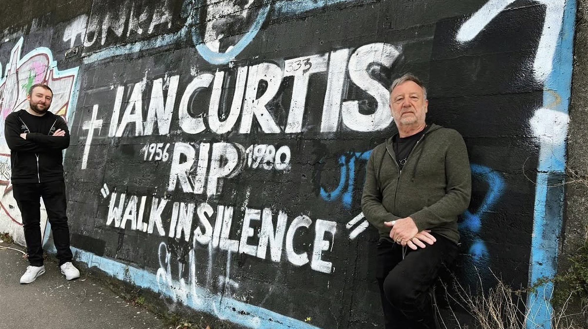 Jack Bates (left) and former Joy Division/New Order bassist Peter Hook of Peter Hook &amp;amp; the Light standing before a mural in tribute to the late Joy Division singer Ian Curtis
