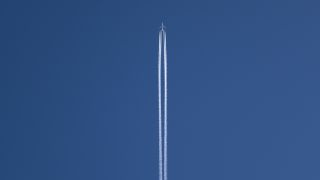 up the center in a vast blue sky two white lines of smoke trail a small airlpaine near the top of the image.