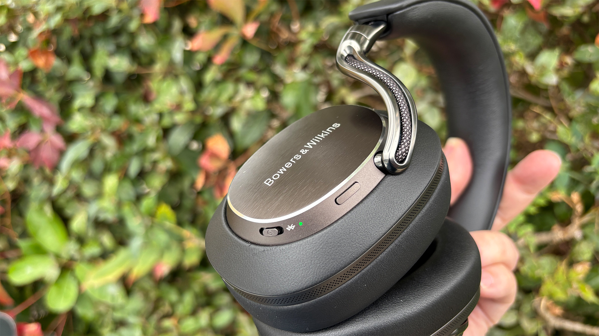 Bowers &amp;amp; Wilkins Px8 S2 wireless headphones held in hand in front of bush showing Bowers &amp;amp; Wilkins logo