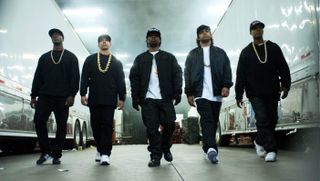 five men in the rap group nwa walking in between two trucks in the movie straight outta compton