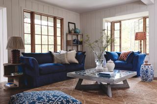 farmhouse style living room with blue sofa and armchair, shiplap walls, rug, coffee table, table lamps