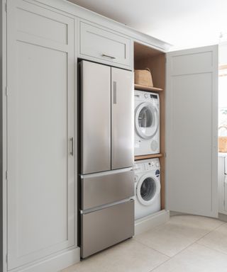 a modern laundry room with gray/green cabinets, a fridge, and a washing machine and dryer hidden behind a cabinet door