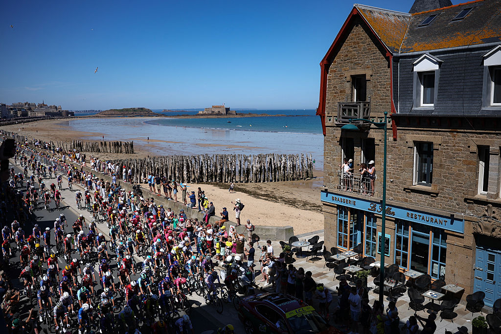 The pack of riders (peloton) cycles along the Saint-Malo coastline at the start of the 7th stage of the 112th edition of the Tour de France cycling race, 197 km between Saint-Malo and Mur-de-Bretagne Guerledan, in Brittany, western France, on July 11, 2025. (Photo by Anne-Christine POUJOULAT / AFP)