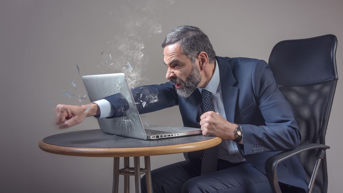 Senior businessman punching a hole through his laptop screen, furious and enraged