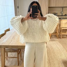 Monikh wears a chunky ivory sweater and ivory pants.