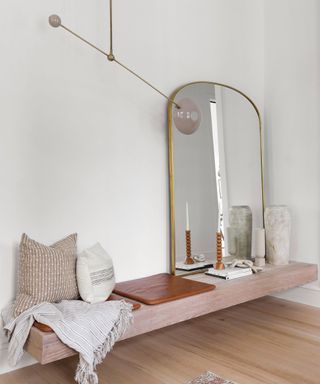 Gold trim mirror on hallway bench styled with cushions, concrete gray vases and accessories