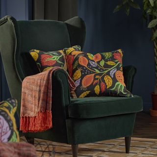 Green velvet chair with fall patterned pillow and throw blanket