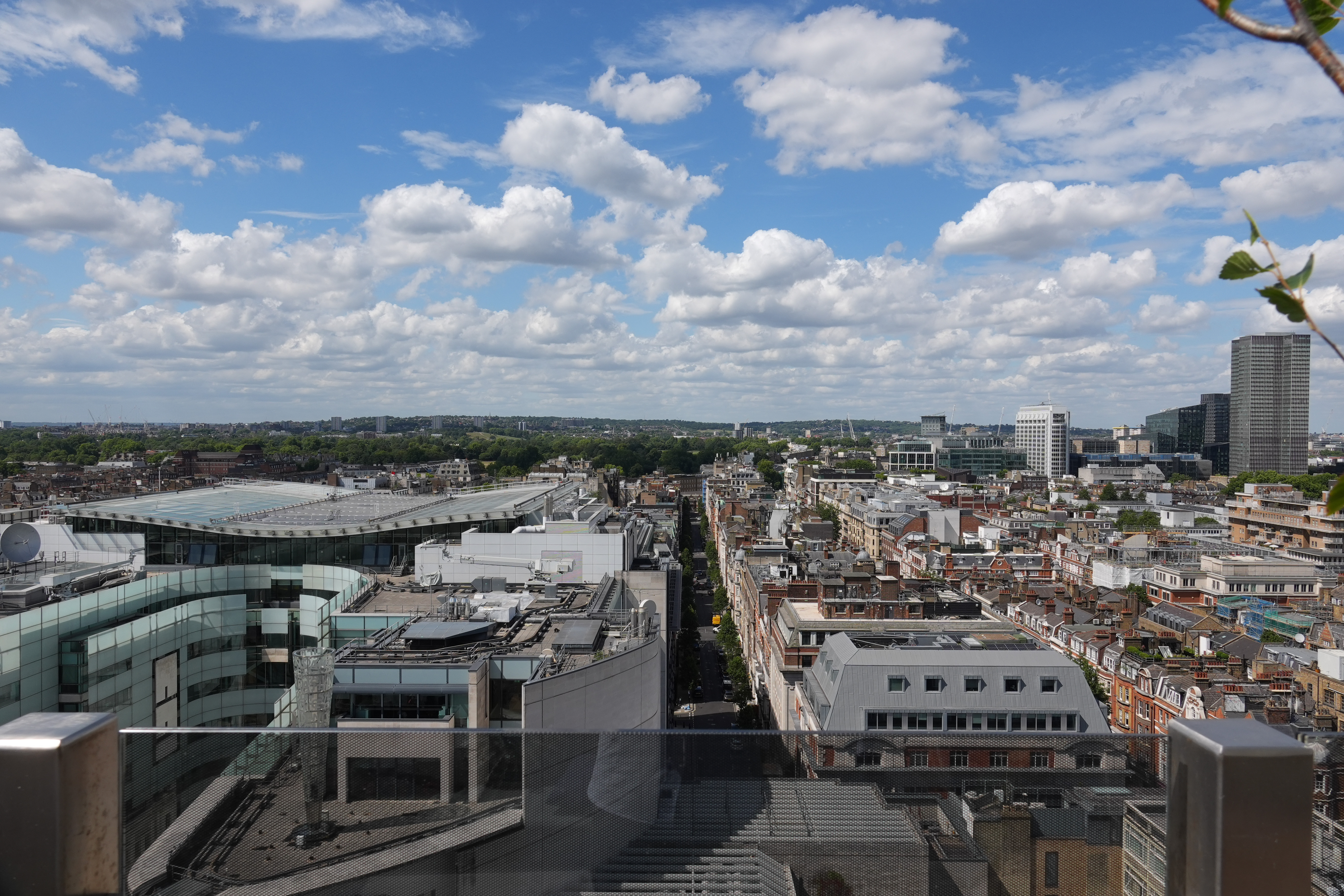 Wide elevated view across central London beneath a bright sky filled with white clouds.