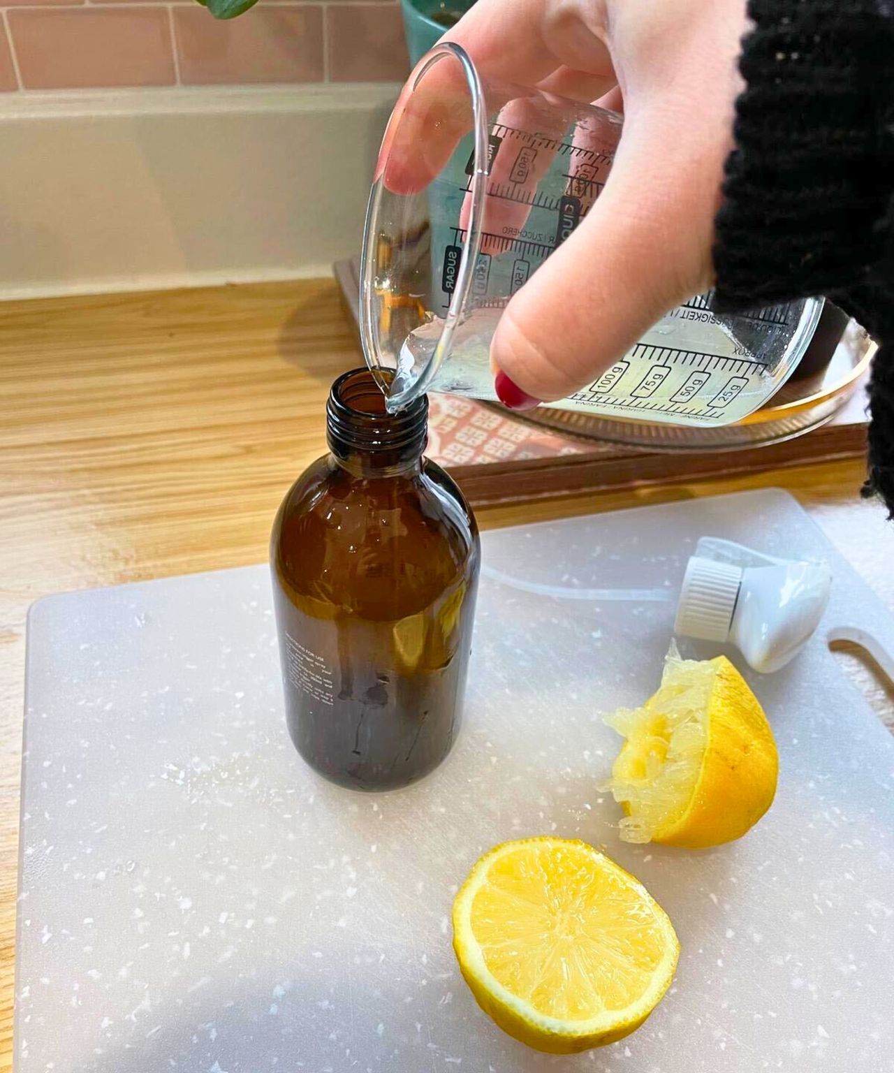 My hand pouring lemon juice and water mix into my amber spray bottle