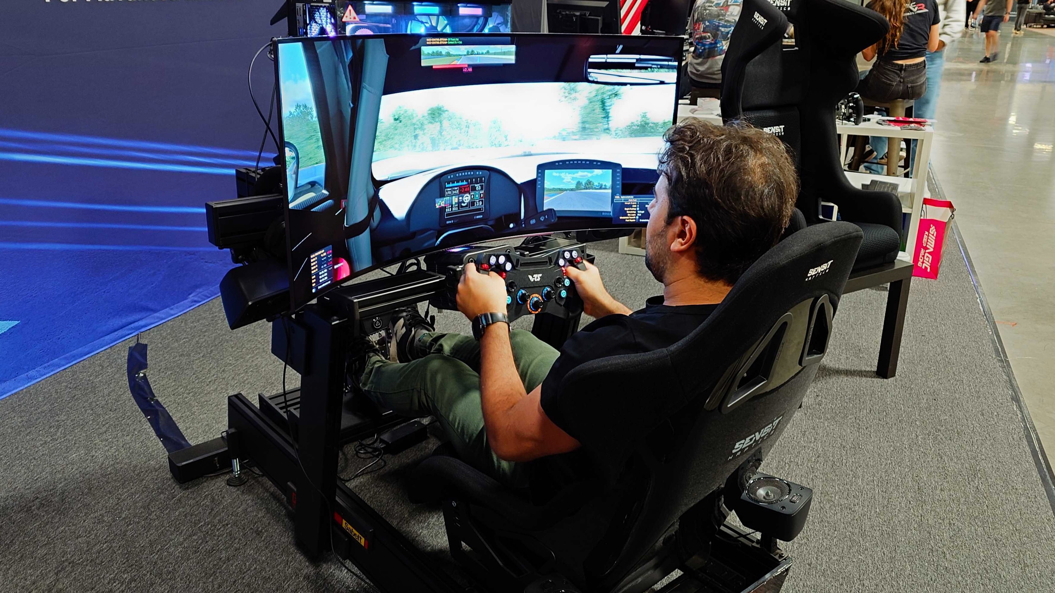 A photo of a person playing iRacing using a wheel and pedal setup sat in a Sensit MTC-P Extreme haptic seat.